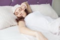 An attractive young brunette girl woman wakes up and sips while yawning in her bed in a sleep mask Royalty Free Stock Photo