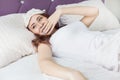 An attractive young brunette girl woman wakes up and sips while yawning in her bed in a sleep mask Royalty Free Stock Photo