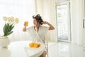 Attractive young brunette woman in hair curlers enjoying orange fresh squeezed juice stretching after sleep in bright Royalty Free Stock Photo