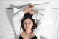 Attractive young brunette woman in snow-white shirt and black bra is lying in bed, top view. Female model in Royalty Free Stock Photo