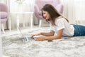 Attractive young brunette woman wearing jeans and white t-shirt lying on the floor in bright livingroom with her laptop