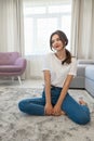 Attractive young brunette woman wearing jeans and white t-shirt sitting on the floor in bright livingroom