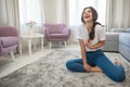 Attractive young brunette woman wearing jeans and white t-shirt sitting on the floor in bright livingroom and bursting