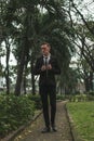 Attractive young business man in black formal suit walking in the park. Royalty Free Stock Photo