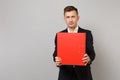 Attractive young business man in classic black suit, shirt holding red folder for papers document isolated on grey Royalty Free Stock Photo