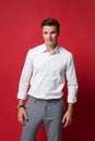 Attractive young business man in white shirt, gray pants posing isolated on bright red wall background studio portrait Royalty Free Stock Photo