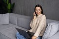 Attractive young business woman relaxing on a leather couch at home, working on laptop computer, talking on mobile phone Royalty Free Stock Photo