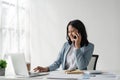 Attractive young business woman talking on the mobile phone and smiling while sitting at her working place in office and Royalty Free Stock Photo