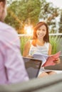 Attractive young business woman holding a file and smiling whilst she has a meeting outside wth a colleague who is working on his