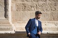 Attractive young businessman with beard and suit, posing leaning against a stone wall. Concept beauty, fashion, success, achiever