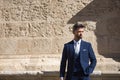 Attractive young businessman with beard and suit, posing next to a stone wall. Concept beauty, fashion, success, achiever, trend