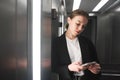 Attractive young businesswoman is looking at her smartphone srreen in the elevator while listening to music. Portrait of employee Royalty Free Stock Photo