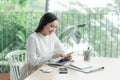 Attractive young businesswoman smiling while sitting alone at her desk in a modern office working online with a digital tablet Royalty Free Stock Photo