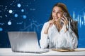 Attractive young businesswoman talking on the phone at desk with candlestick forex chart hologram, laptop and supplies. Finance, Royalty Free Stock Photo