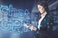 Attractive businesswoman using tablet with glowing chat gpt hologram on blurry office interior background. AI, futuristic Royalty Free Stock Photo