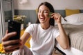 Attractive young caucasian brunette girl massages her face and laughs at smartphone camera.