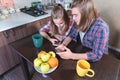 An attractive young Caucasian couple in the kitchen at the dinner table drinks tea and uses their smartphones. Royalty Free Stock Photo