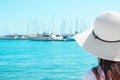 Attractive Young Caucasian Woman with Long Hair in Hat Stands at Beach Looks at Yachts Sailing Boats Moored in Marina Royalty Free Stock Photo