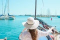 Attractive Young Caucasian Woman with Long Hair in Hat Stands in Vintage Sailing Boat Looks at Yachts Moored in Marina