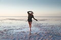 Attractive young Caucasian woman in a straw hat and long jacket walks balancing on a shallow salt lake at sunset Royalty Free Stock Photo