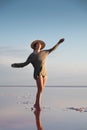 Attractive young Caucasian woman in a straw hat and long jacket walks balancing on a shallow salt lake at sunset Royalty Free Stock Photo