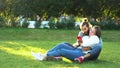 Attractive young couple at the city park sitting on the grass, hugging and looking at smartphone. Concept. Loving man Royalty Free Stock Photo