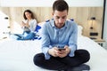 Attractive young couple ignoring each other using phone after an argument while sitting on bed at hotel room Royalty Free Stock Photo