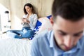 Attractive young couple ignoring each other using phone after an argument while sitting on bed at hotel room Royalty Free Stock Photo