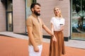 Attractive young couple in love standing holding hands on city street, cheerful looking. Handsome bearded man with Royalty Free Stock Photo