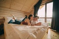 Attractive young couple lying on a sofa in a wooden apartment and using a smartphone. Young man and attractive woman relaxing in a