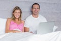Attractive young couple using their laptop together in bed Royalty Free Stock Photo