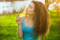 Attractive, young, curly girl in blue shirt, holding a dandelion blooming and smiling. Royalty Free Stock Photo