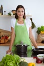 An attractive young dark-haired woman preparing soup by new keto recipe while standing and smiling in the kitchen Royalty Free Stock Photo