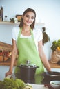 An attractive young dark-haired woman preparing soup by new keto recipe while standing and smiling in the kitchen Royalty Free Stock Photo