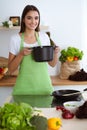 An attractive young dark-haired woman preparing soup by new keto recipe while standing and smiling in the kitchen Royalty Free Stock Photo