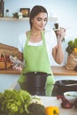 An attractive young dark-haired woman preparing soup by new keto recipe while standing and smiling in the kitchen Royalty Free Stock Photo