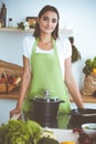 An attractive young dark-haired woman preparing soup by new keto recipe while standing and smiling in the kitchen Royalty Free Stock Photo