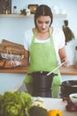 An attractive young dark-haired woman preparing soup by new keto recipe while standing and smiling in the kitchen Royalty Free Stock Photo