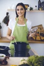 An attractive young dark-haired woman preparing soup by new keto recipe while standing and smiling in the kitchen Royalty Free Stock Photo