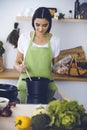 An attractive young dark-haired woman preparing soup by new keto recipe while standing and smiling in the kitchen Royalty Free Stock Photo