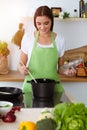 An attractive young dark-haired woman preparing soup by new keto recipe while standing and smiling in sunny kitchen