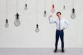 Attractive young european businessman showing power muscle while standing in simple concrete interior with many hanging light