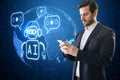 Attractive young european businessman with smartphone and creative glowing robot and globe ai hologram on blurry background.