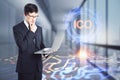 Attractive young european businessman using laptop in blurry office interior with ICO hologram. Initial coin offering and Royalty Free Stock Photo