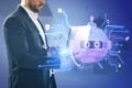 Attractive young european businessman using laptop computer with creative robot hologram on blurry office interior background. Royalty Free Stock Photo