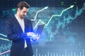Attractive young european businessman using laptop computer with growing upward chart, map, arrows and forex graph on blurry