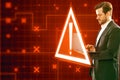 Attractive european businessman using laptop with creative red security alert on blurry background. Fraud and danger concept Royalty Free Stock Photo