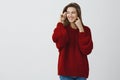 Attractive young female student adoring beautiful snowy days looking out window in red loose sweater turning left