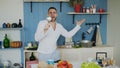 Attractive young funny man dancing and singing with ladle while cooking in the kitchen at home Royalty Free Stock Photo