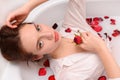 Attractive young girl in a bath with milk and red rose petals. The concept of pleasure, relaxation and romance Royalty Free Stock Photo